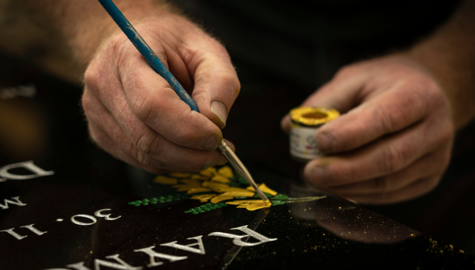 Painting kōwhai flowers onto a granite memorial
